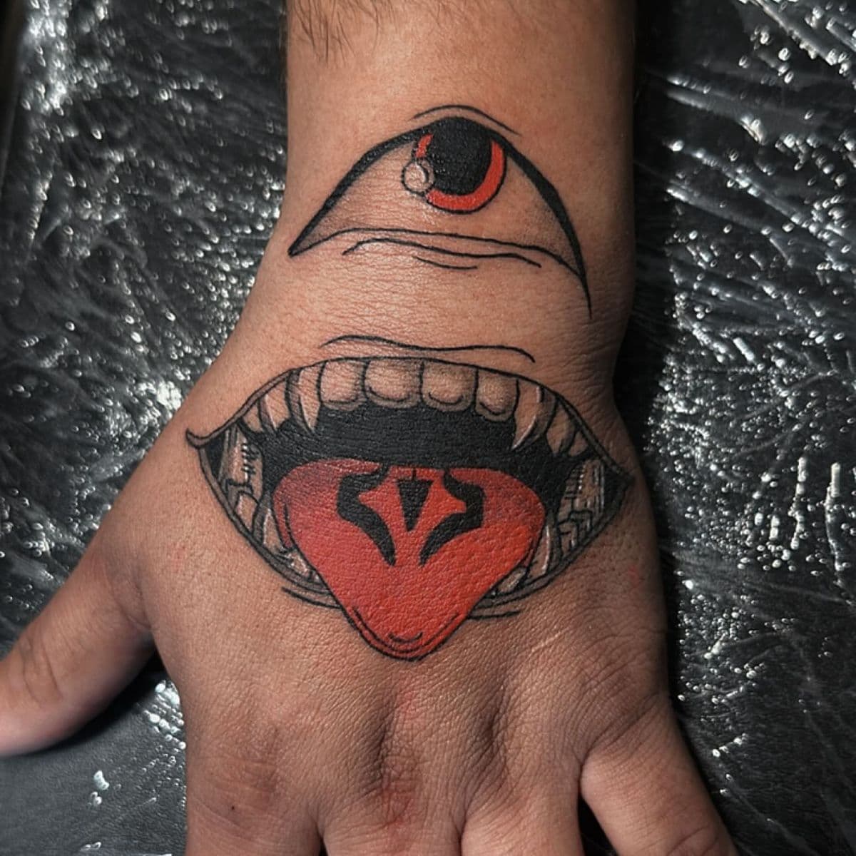 Traditional all-seeing eye and open fang mouth hand tattoo