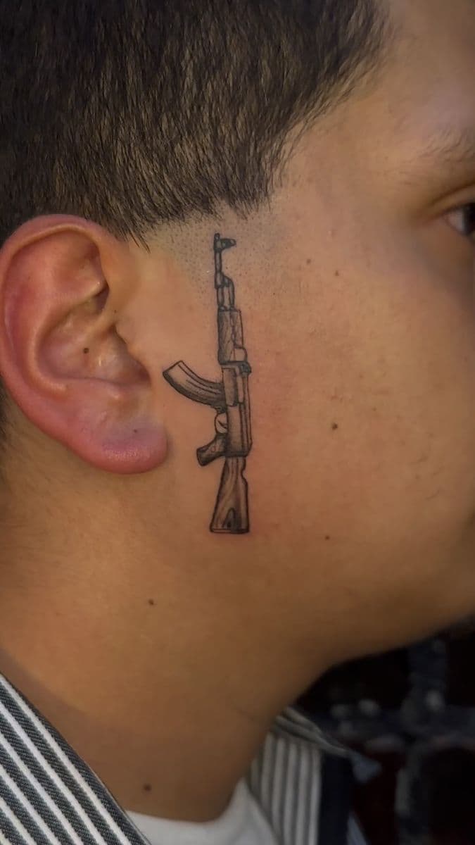 AK-47 fine line tattoo behind the ear